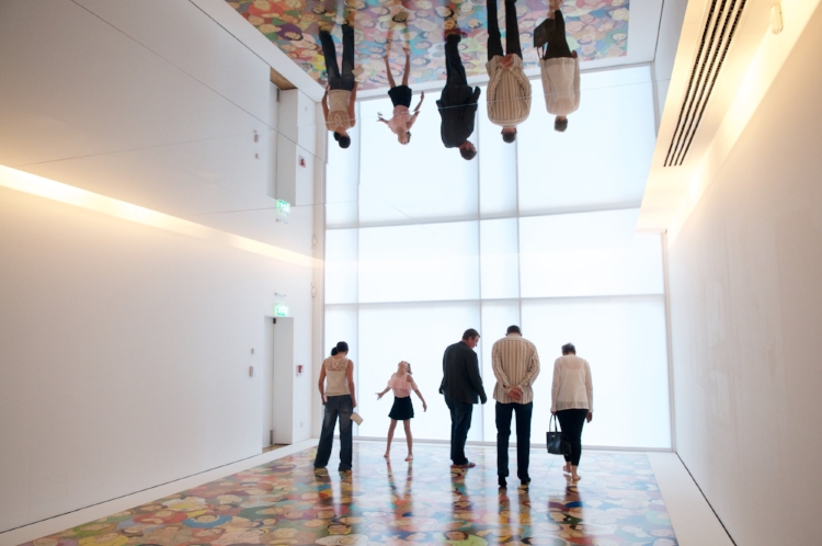 Image of a group enjoying an exhibit by artist NS Harsha at the Glynn Vivian Art Gallery. Four adults look at an image on the floor while a child looks up at the reflection on the ceiling