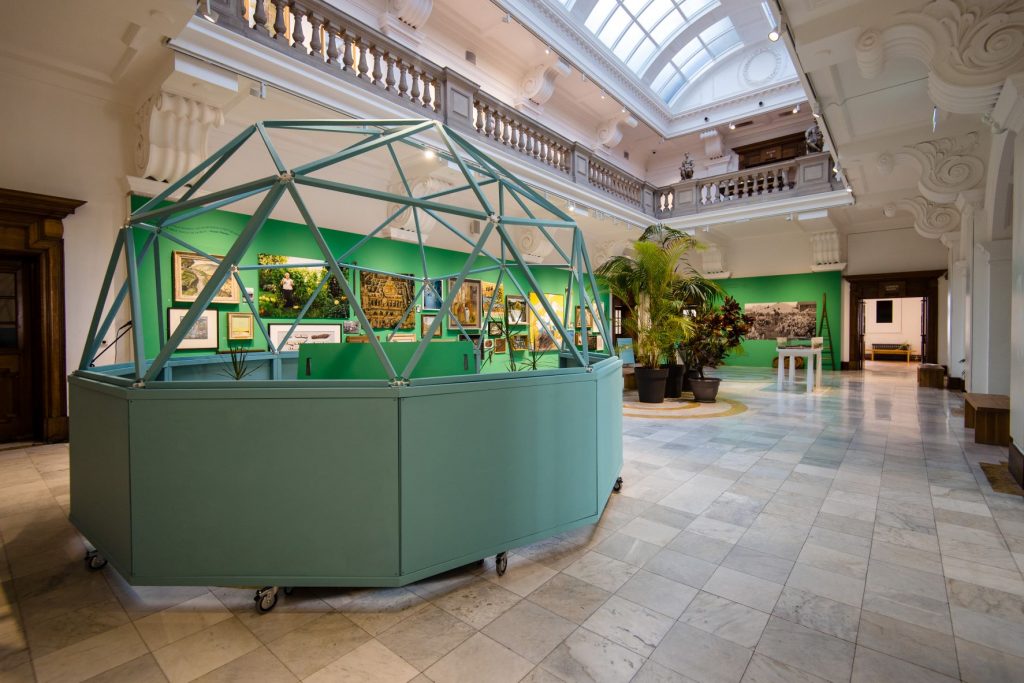 Glynn Vivian Gallery Atrium space, in the foreground is a light green open geodome. In the background there is a green wall, with paintings and objects hung for the exhibition, Thinking Green, by artist Owen Griffiths. 